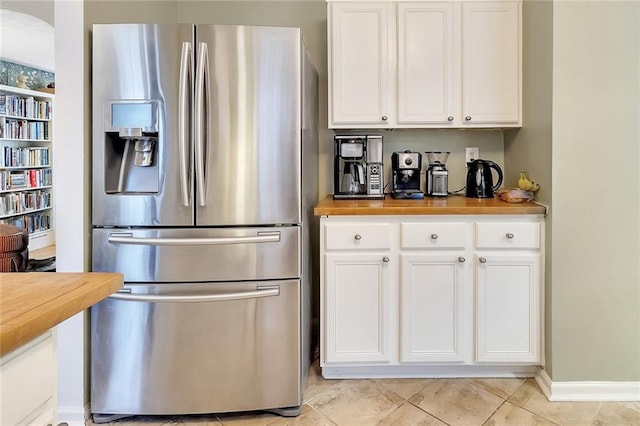 kitchen with white cabinets, stainless steel fridge with ice dispenser, butcher block countertops, and light tile patterned flooring