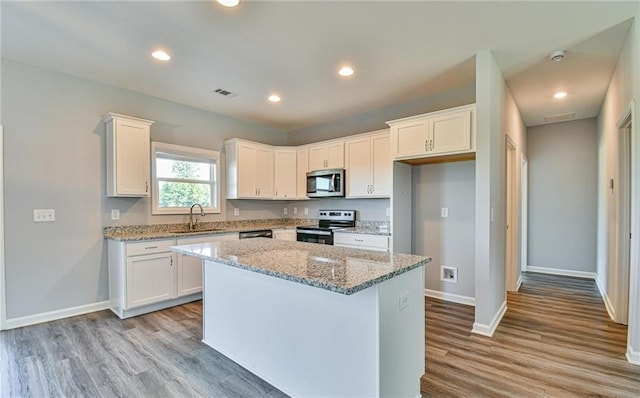 kitchen featuring visible vents, a sink, white cabinets, stainless steel appliances, and light wood-style flooring