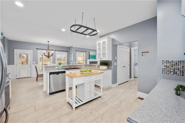 kitchen with glass insert cabinets, a peninsula, a notable chandelier, white cabinets, and stainless steel dishwasher