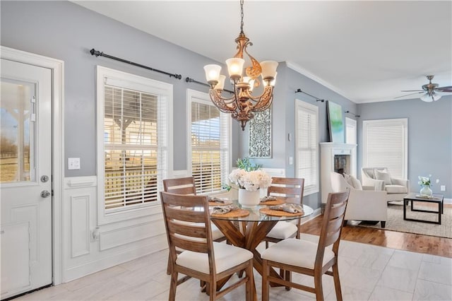 dining space featuring ceiling fan with notable chandelier, crown molding, light wood-style floors, and wainscoting