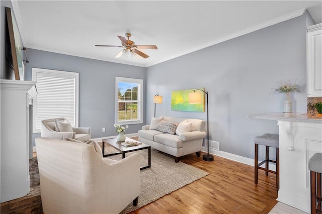 living area with visible vents, crown molding, baseboards, wood finished floors, and a ceiling fan