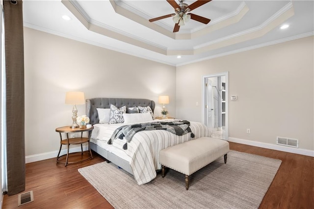 bedroom featuring a tray ceiling, crown molding, wood finished floors, and visible vents