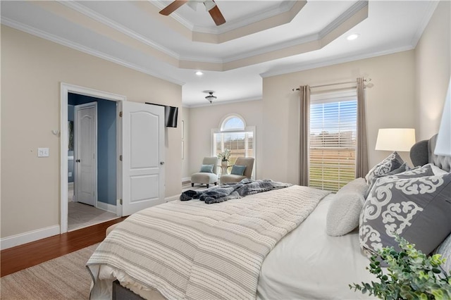 bedroom featuring a tray ceiling, wood finished floors, baseboards, and ornamental molding