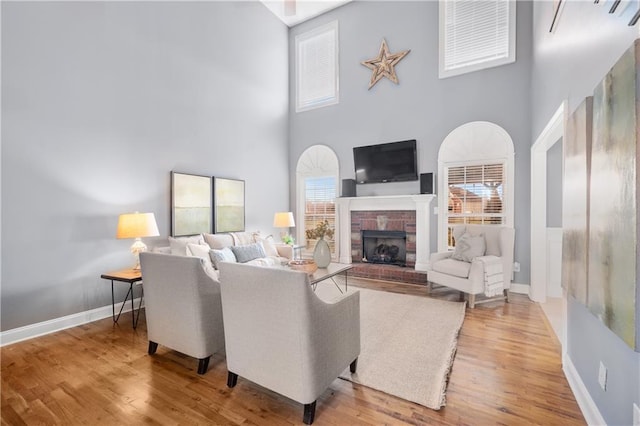 living room with a fireplace, wood finished floors, baseboards, and a towering ceiling