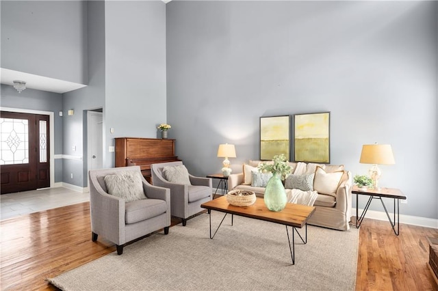 living room with baseboards, light wood-style flooring, and a towering ceiling