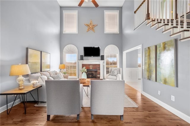 living room featuring wood finished floors, a high ceiling, a fireplace, baseboards, and ceiling fan