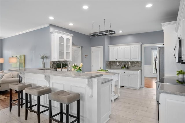 kitchen with tasteful backsplash, glass insert cabinets, a breakfast bar area, appliances with stainless steel finishes, and white cabinetry