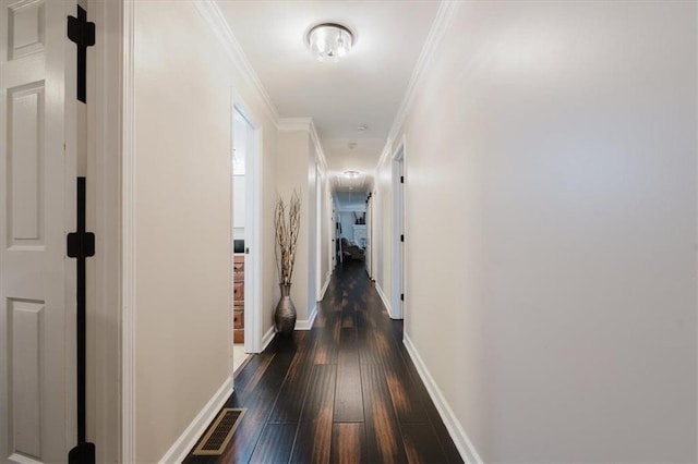 hallway with ornamental molding, baseboards, visible vents, and dark wood-type flooring