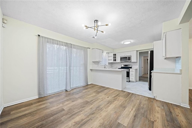 kitchen featuring stainless steel appliances, a peninsula, light countertops, and light wood-style flooring