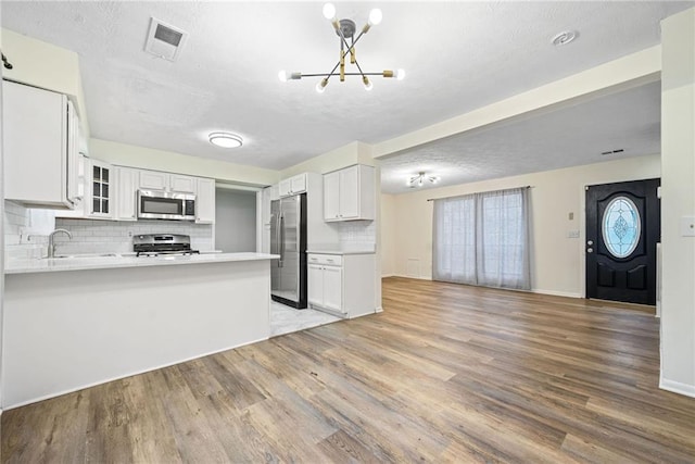 kitchen with visible vents, light wood-style flooring, glass insert cabinets, appliances with stainless steel finishes, and open floor plan