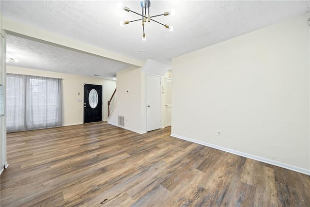 unfurnished living room featuring an inviting chandelier, stairs, baseboards, and wood finished floors