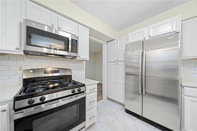 kitchen featuring white cabinets, marble finish floor, tasteful backsplash, and stainless steel appliances