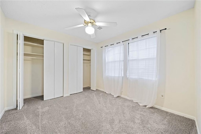 unfurnished bedroom with carpet, baseboards, and two closets