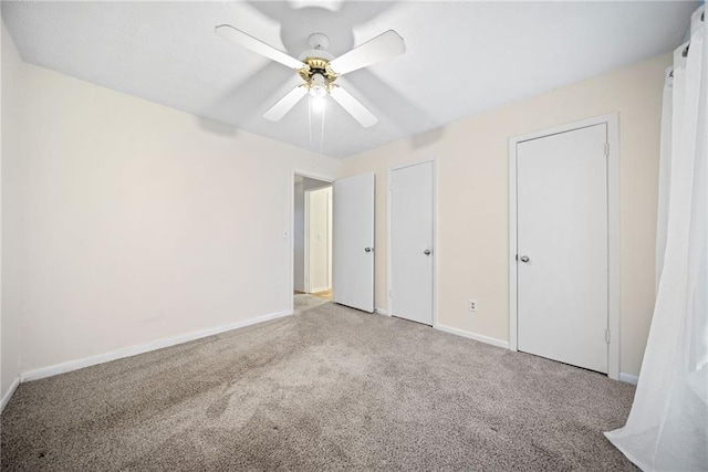 unfurnished bedroom with carpet floors, a ceiling fan, baseboards, and multiple closets