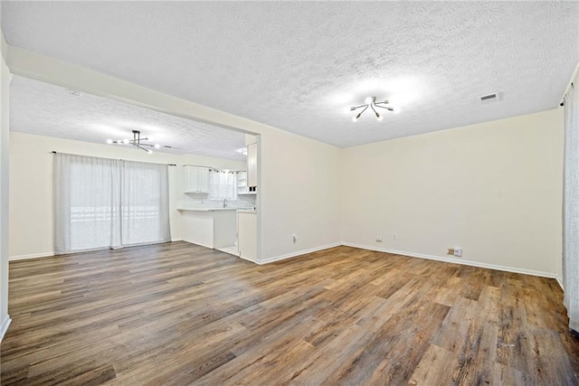 unfurnished living room with visible vents, a textured ceiling, baseboards, and wood finished floors