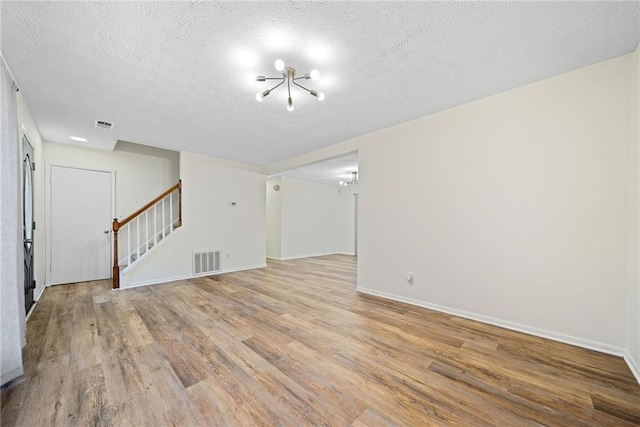 spare room featuring baseboards, visible vents, wood finished floors, stairs, and a textured ceiling