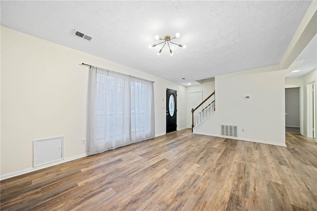 interior space with stairs, a textured ceiling, wood finished floors, and visible vents