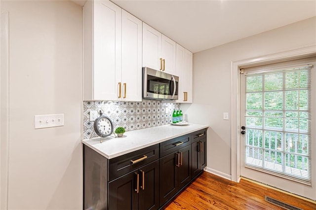 kitchen featuring tasteful backsplash, visible vents, stainless steel microwave, light countertops, and white cabinetry