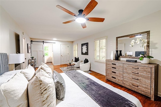 bedroom featuring a barn door, baseboards, ceiling fan, and wood finished floors