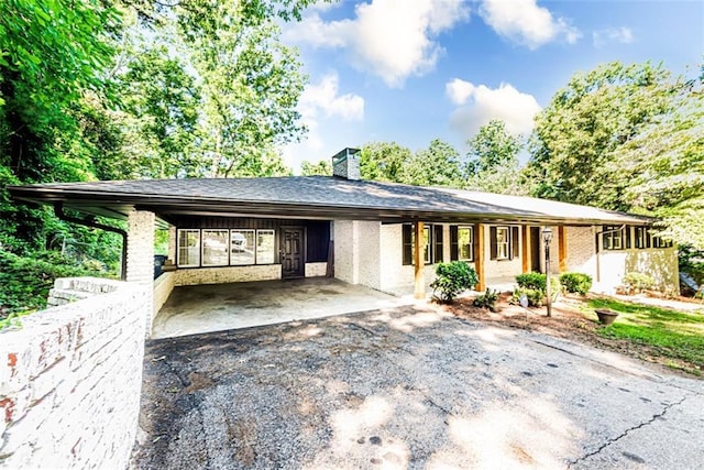 view of front of home featuring driveway, a chimney, a carport, and brick siding