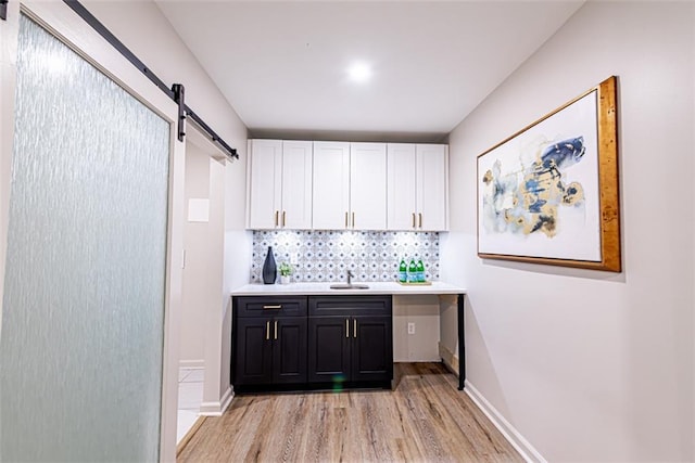 bar with a barn door, a sink, baseboards, light wood-type flooring, and decorative backsplash