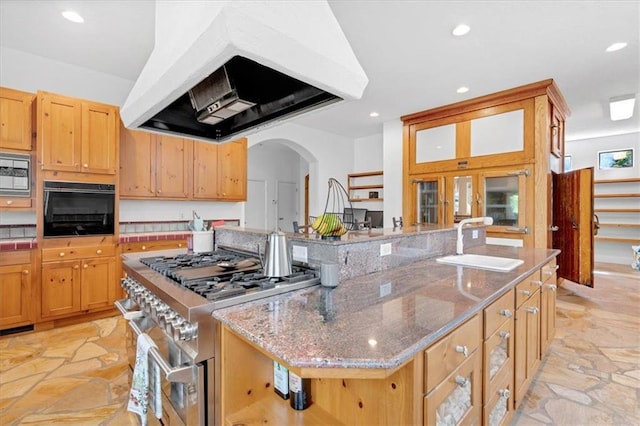 kitchen with custom exhaust hood, stainless steel appliances, light stone counters, sink, and a kitchen island