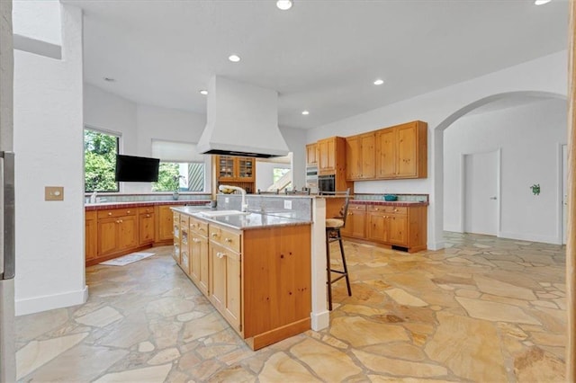 kitchen featuring a kitchen bar, custom range hood, sink, and a kitchen island with sink