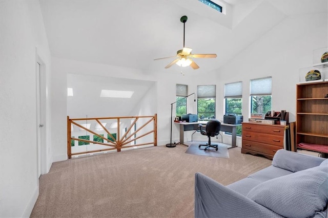 carpeted home office with ceiling fan, high vaulted ceiling, and a skylight