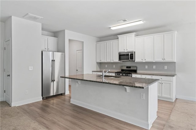 kitchen with sink, stainless steel appliances, an island with sink, white cabinets, and dark stone counters