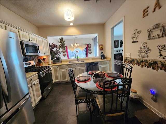 kitchen with sink, hanging light fixtures, a textured ceiling, appliances with stainless steel finishes, and a notable chandelier