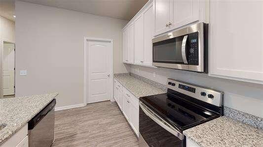 kitchen with white cabinetry, light stone counters, light wood finished floors, and stainless steel appliances