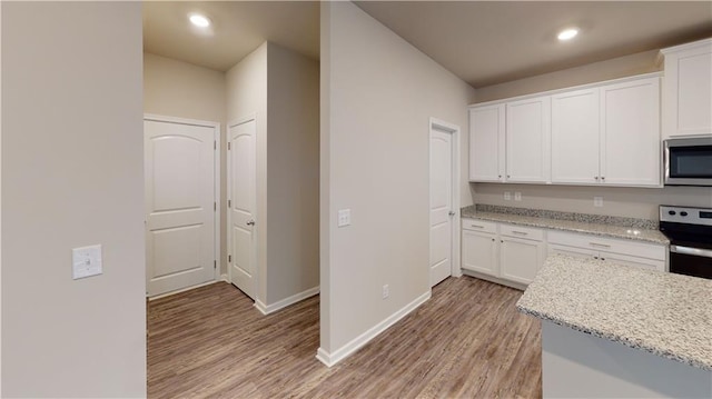 kitchen featuring light stone countertops, baseboards, light wood-style flooring, white cabinets, and appliances with stainless steel finishes