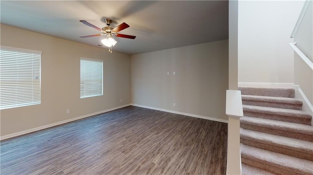 empty room featuring stairway, wood finished floors, baseboards, and ceiling fan