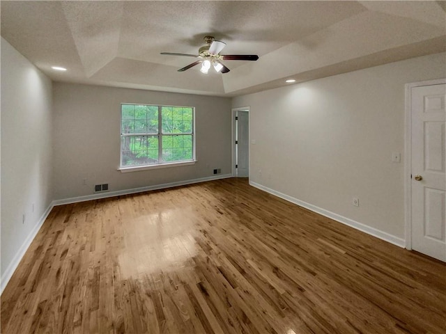 empty room with ceiling fan, hardwood / wood-style flooring, and a tray ceiling