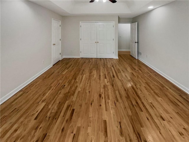 unfurnished bedroom featuring ceiling fan, light hardwood / wood-style floors, and a raised ceiling