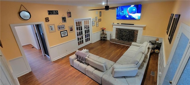 living area with wainscoting, a brick fireplace, a ceiling fan, and wood finished floors