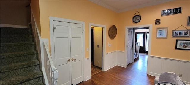 stairs featuring wood finished floors, ornamental molding, and wainscoting