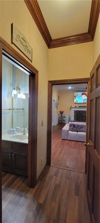 hallway with dark wood finished floors, ornamental molding, baseboards, and a sink