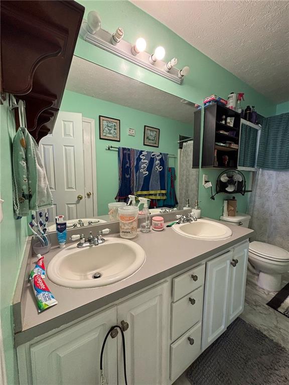 bathroom featuring double vanity, a textured ceiling, toilet, and a sink