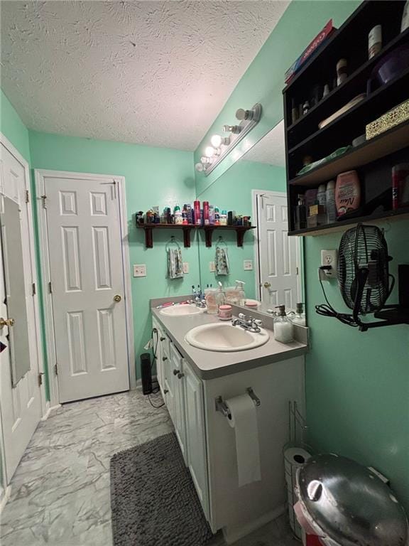 bathroom featuring marble finish floor, a sink, a textured ceiling, and double vanity