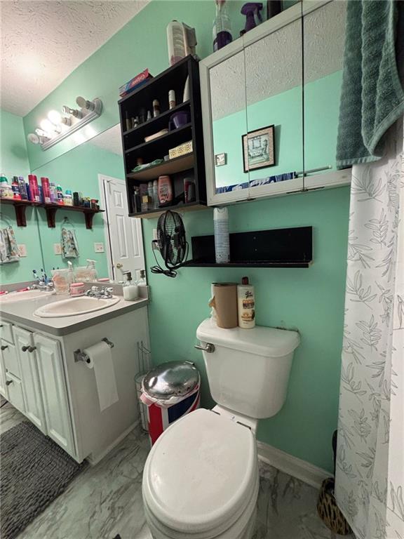 bathroom featuring marble finish floor, a textured ceiling, toilet, and vanity