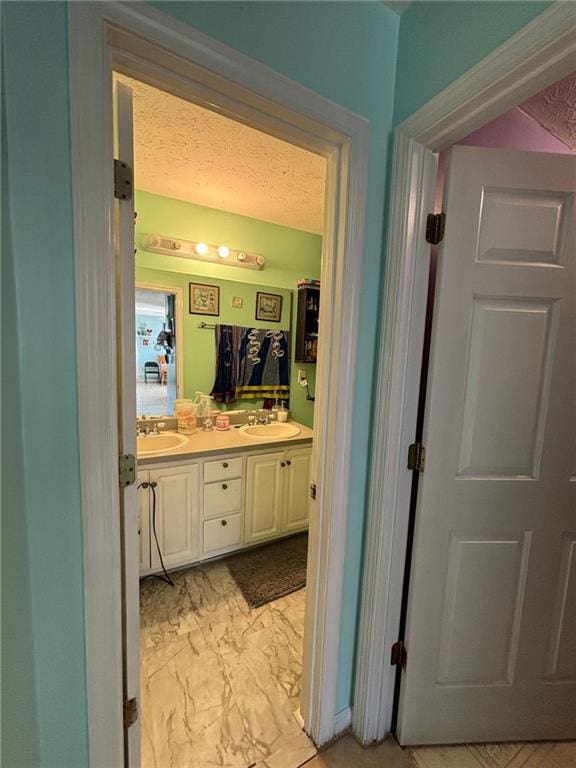 bathroom featuring double vanity, marble finish floor, a textured ceiling, and a sink