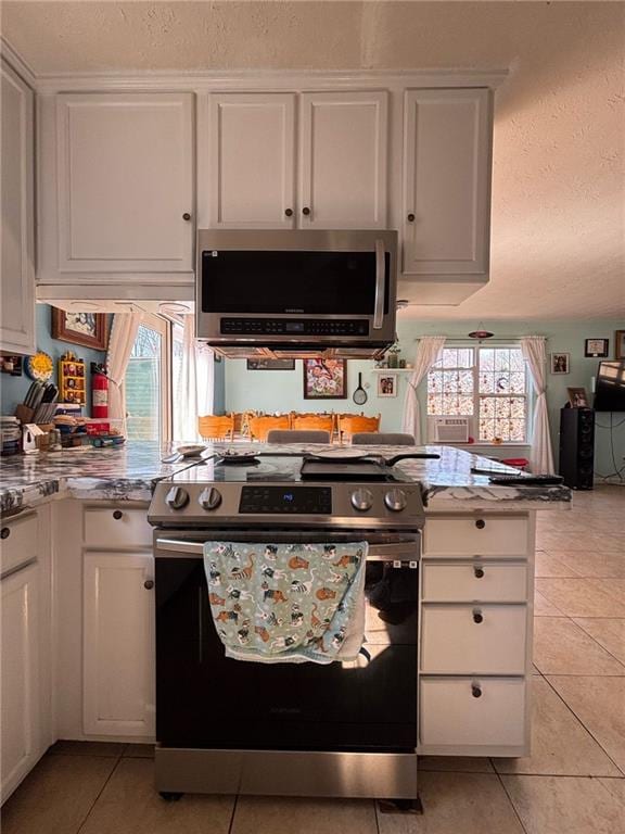 kitchen with light tile patterned floors, appliances with stainless steel finishes, a healthy amount of sunlight, and white cabinets