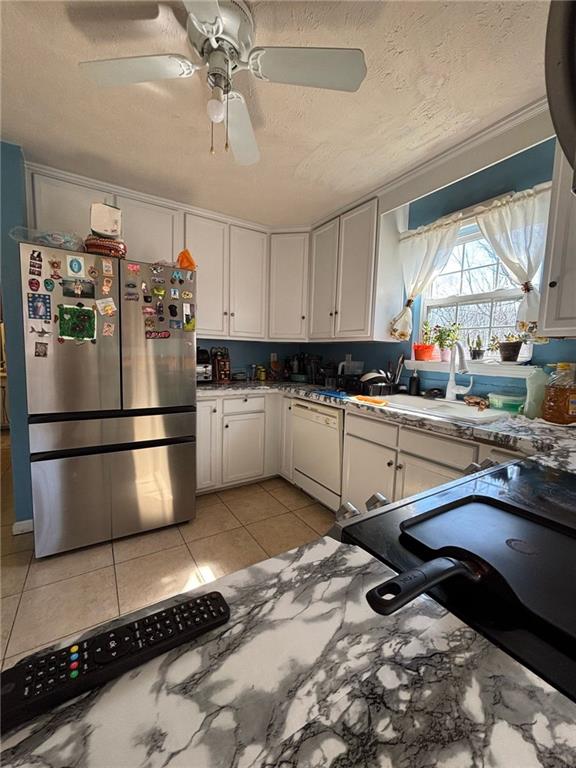 kitchen featuring freestanding refrigerator, white cabinetry, a sink, a textured ceiling, and dishwasher