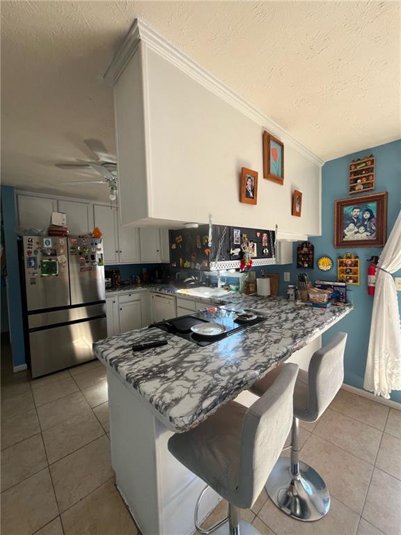 kitchen with light tile patterned floors, a ceiling fan, freestanding refrigerator, a textured ceiling, and a peninsula