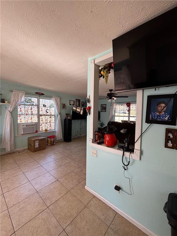 interior space featuring a ceiling fan, light tile patterned flooring, a textured ceiling, and baseboards