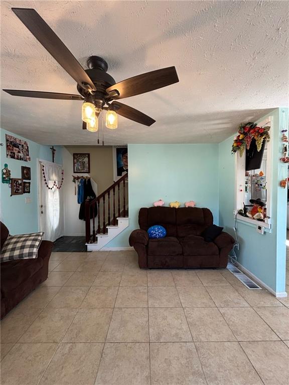 living room with light tile patterned floors, stairway, ceiling fan, a textured ceiling, and baseboards