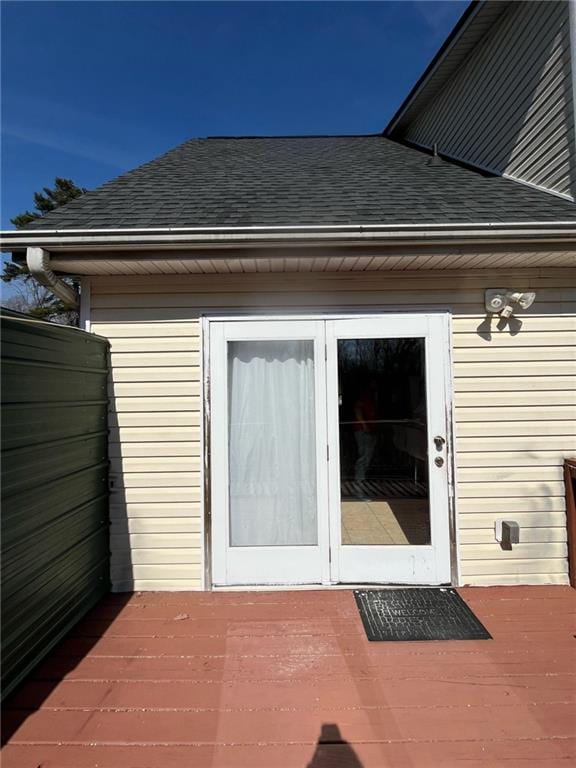 entrance to property featuring roof with shingles and a wooden deck