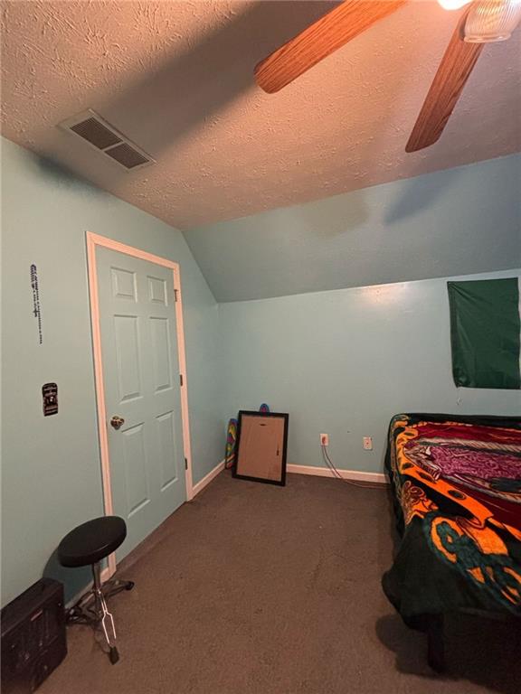 carpeted bedroom featuring a textured ceiling, vaulted ceiling, visible vents, and baseboards