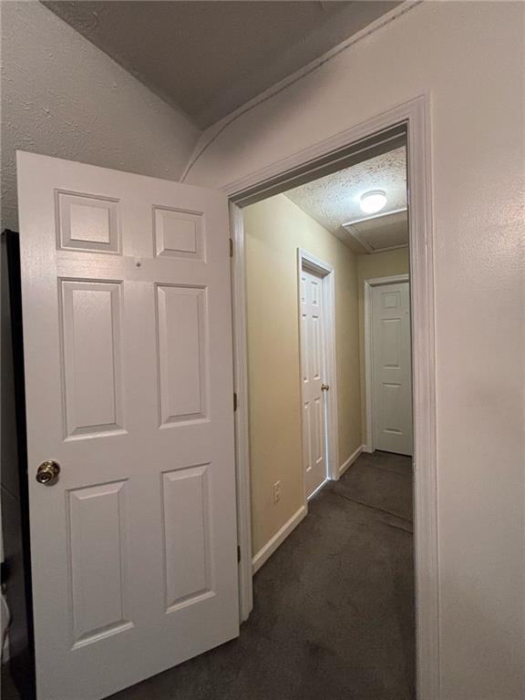 corridor featuring a textured ceiling, dark carpet, and baseboards